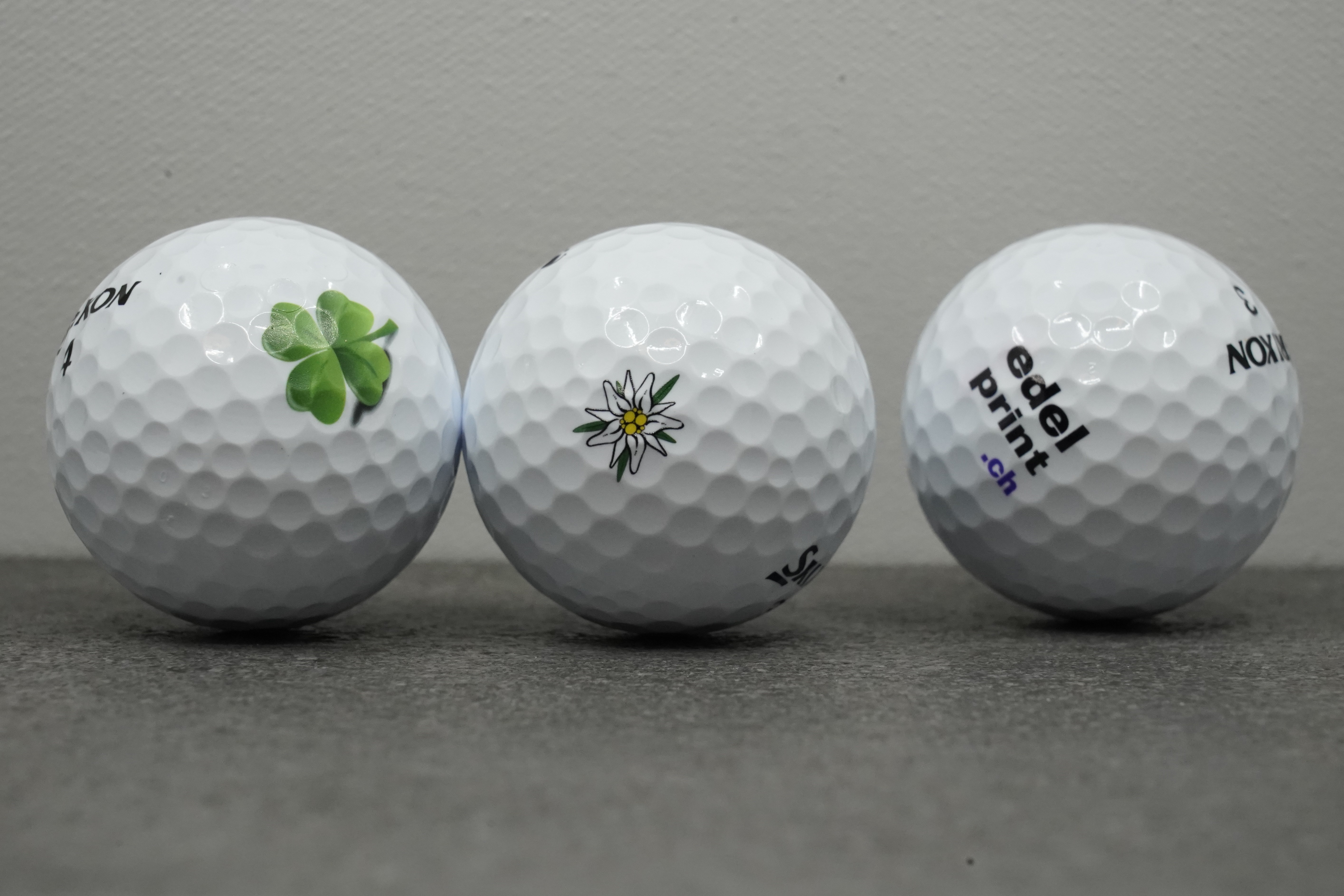 Drei Golfbälle mit UV-Direktdruck: Kleeblatt, Edelweiss, edelprint.ch-Logo
